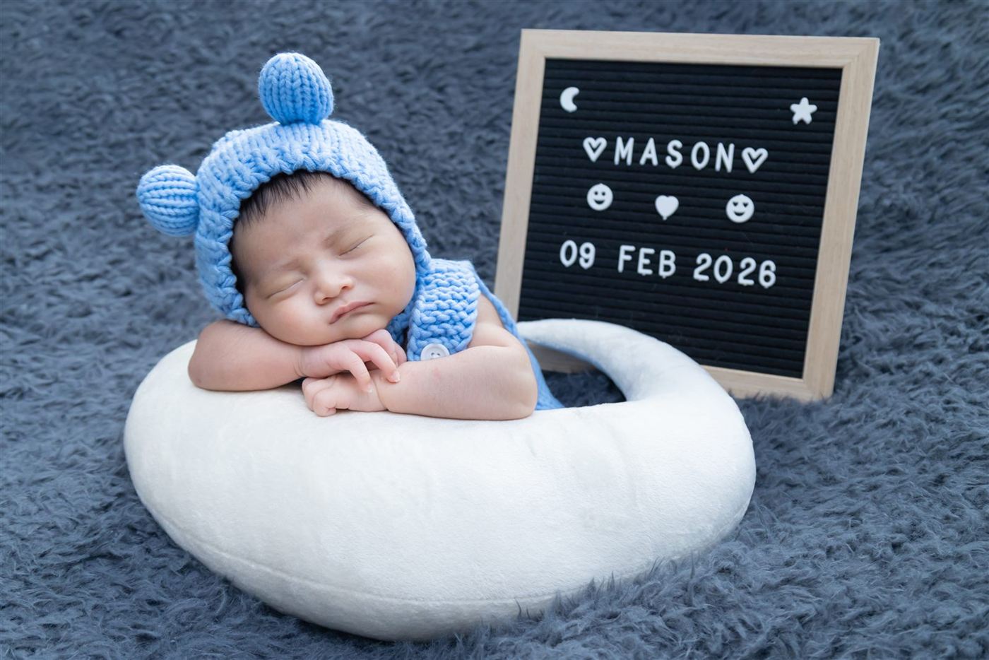Newborn in a blue bear bonnet beside a name letterboard