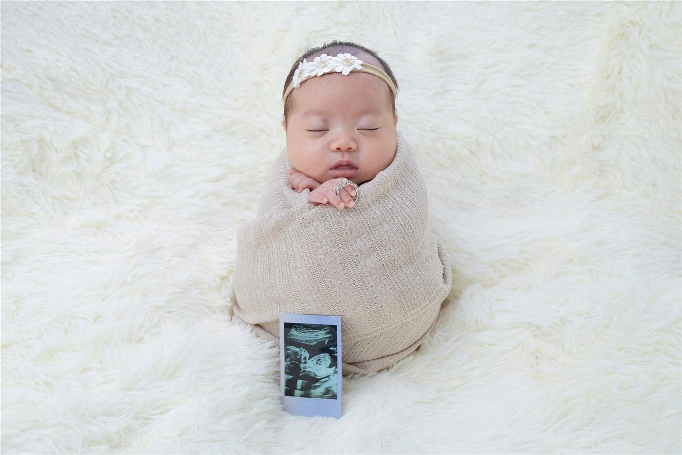 Newborn with a floral headband beside an ultrasound photo