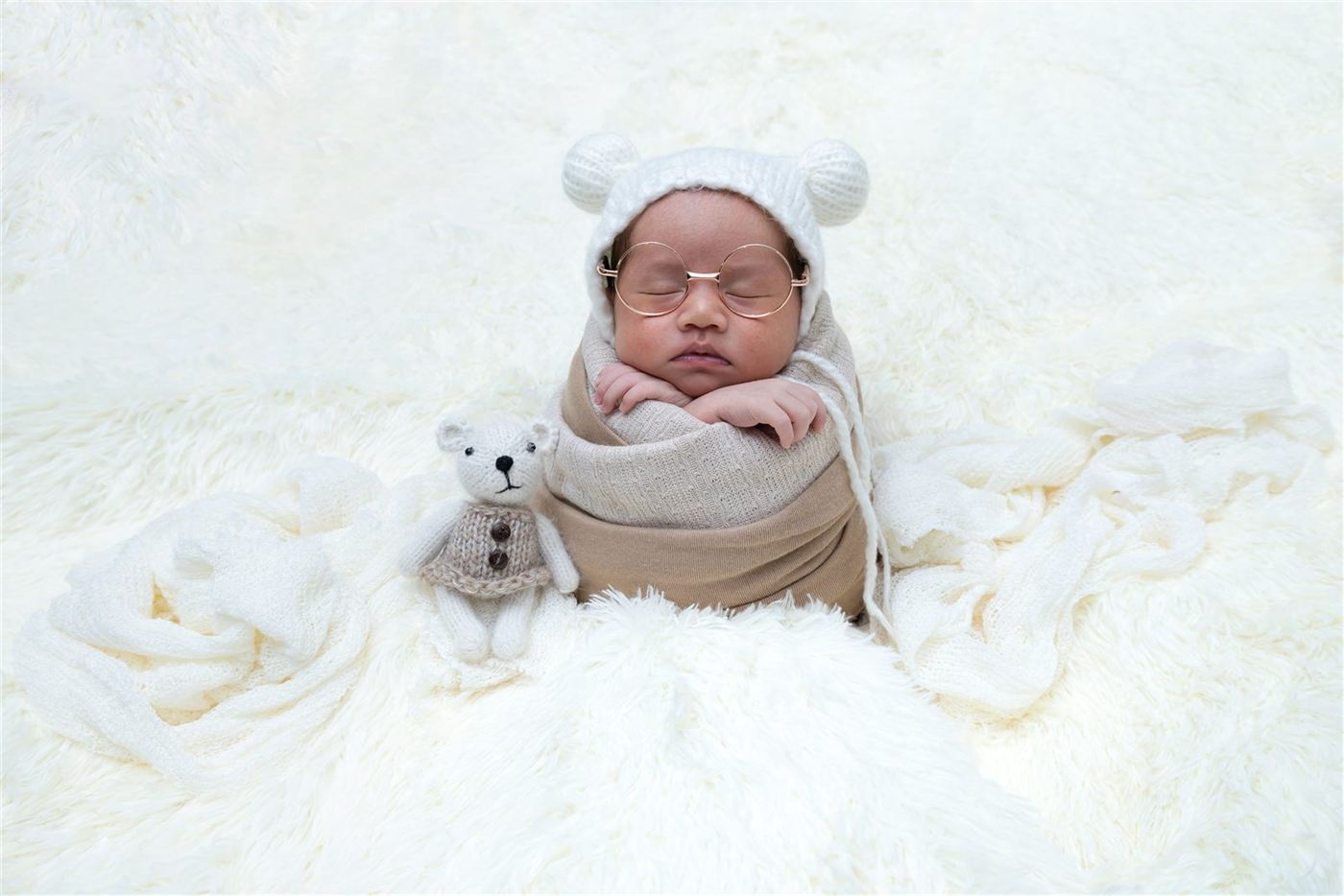 Newborn in a bear bonnet and round glasses with a teddy
