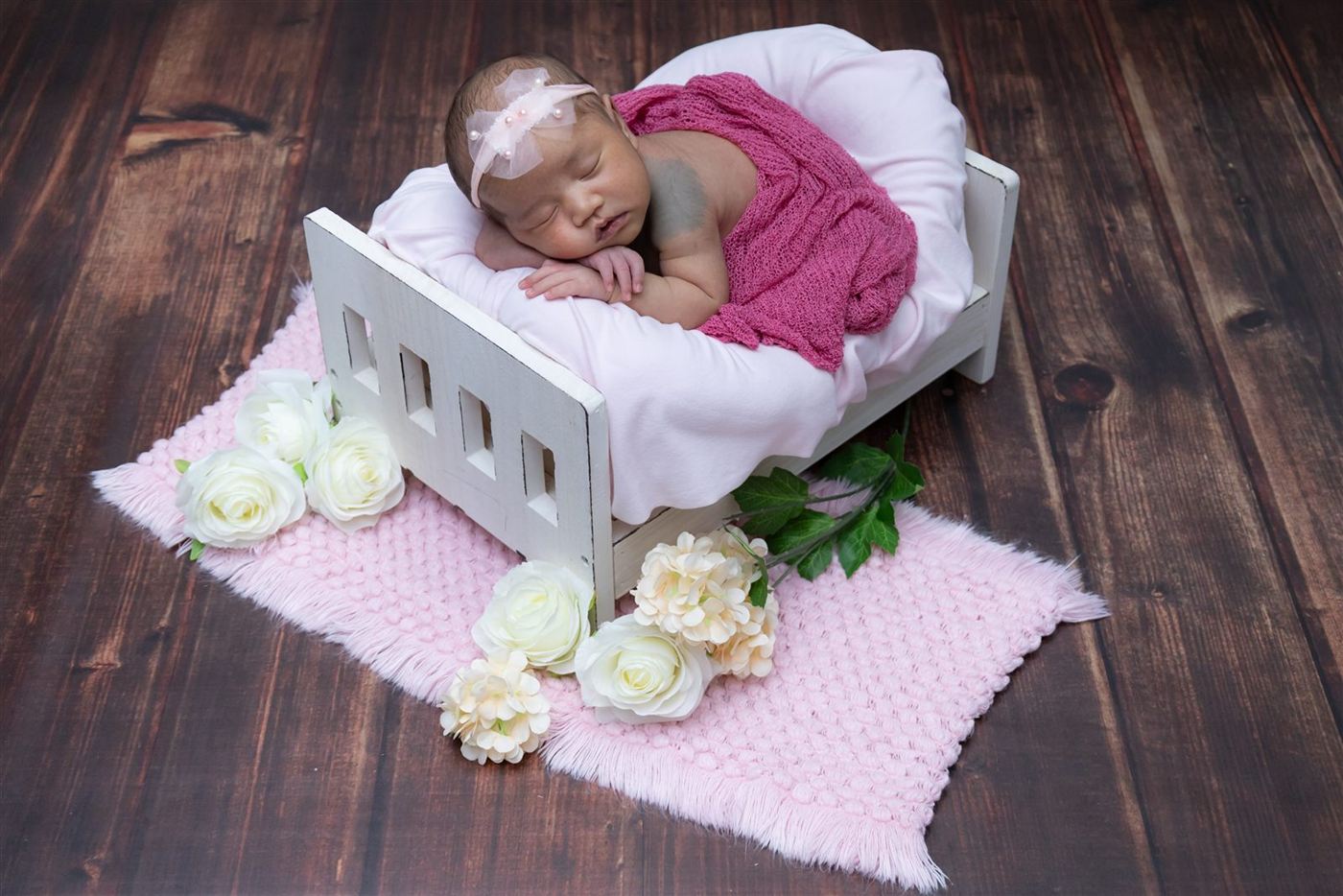 Newborn in a white crib with a pink wrap and roses